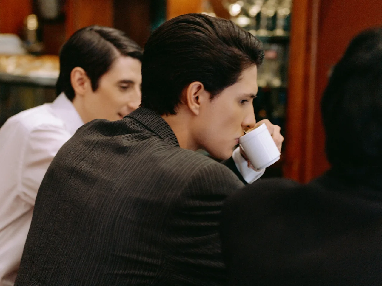 Two men with dark groomed hair drinking espresso at a café counter