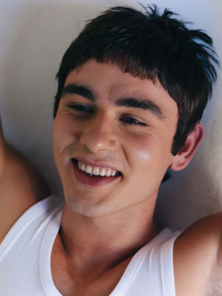Smiling man with dark hair in a white t-shirt resting in soft daylight