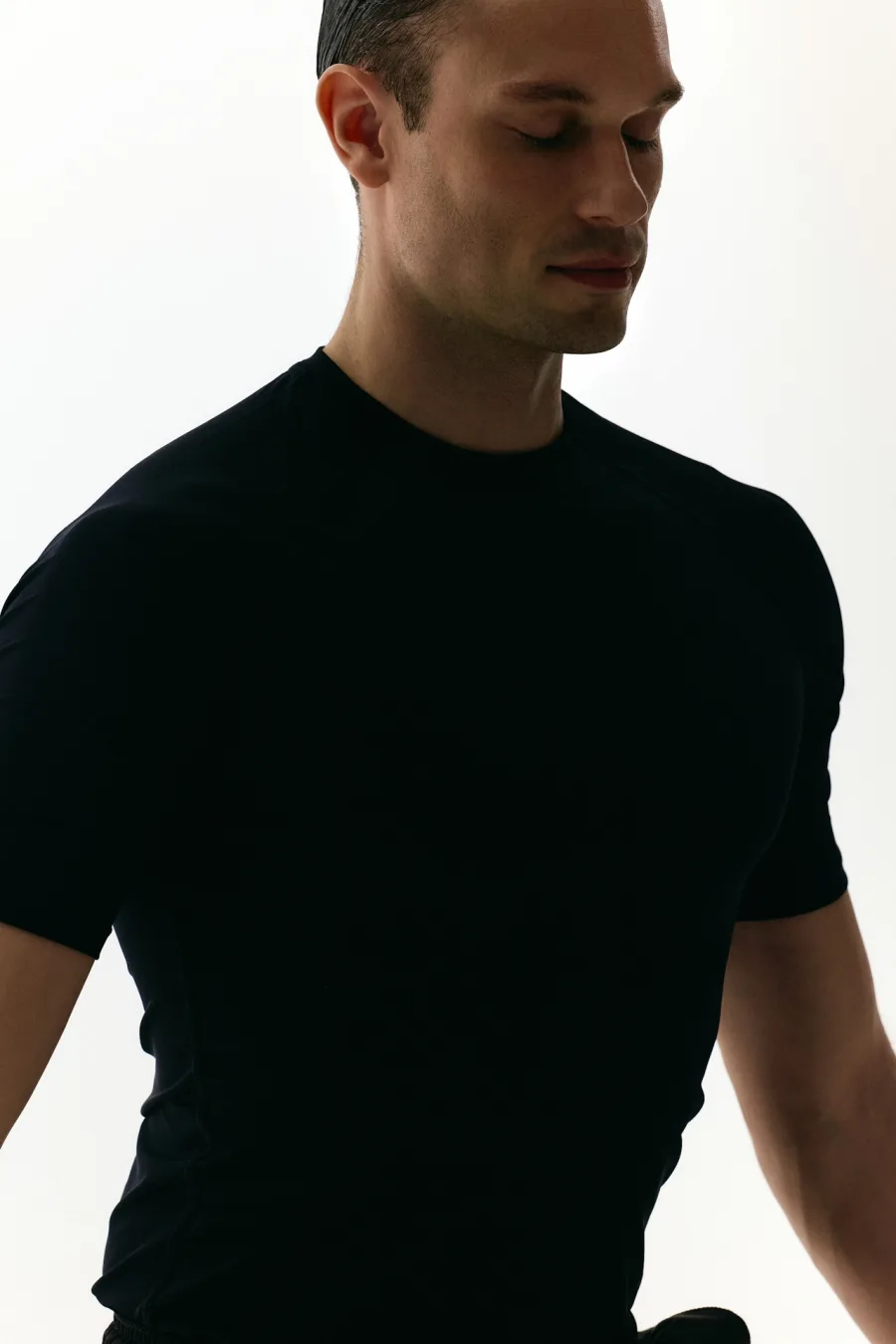 Man in a fitted black t-shirt looking down in soft studio light